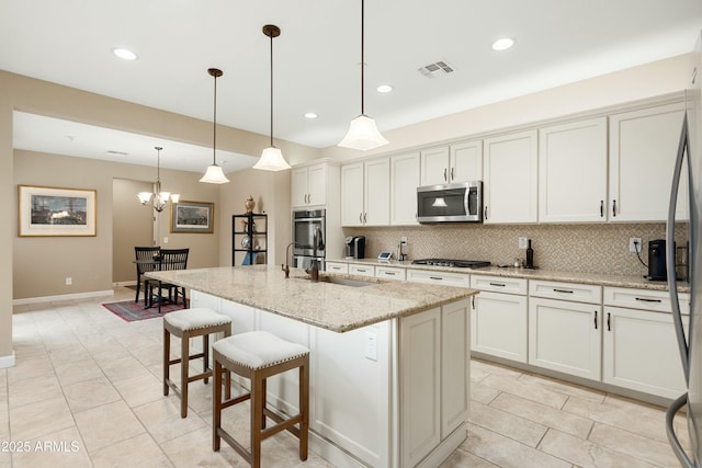 kitchen featuring visible vents, decorative backsplash, appliances with stainless steel finishes, a kitchen breakfast bar, and light stone countertops