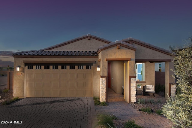 view of front facade with a tiled roof, decorative driveway, an attached garage, and stucco siding
