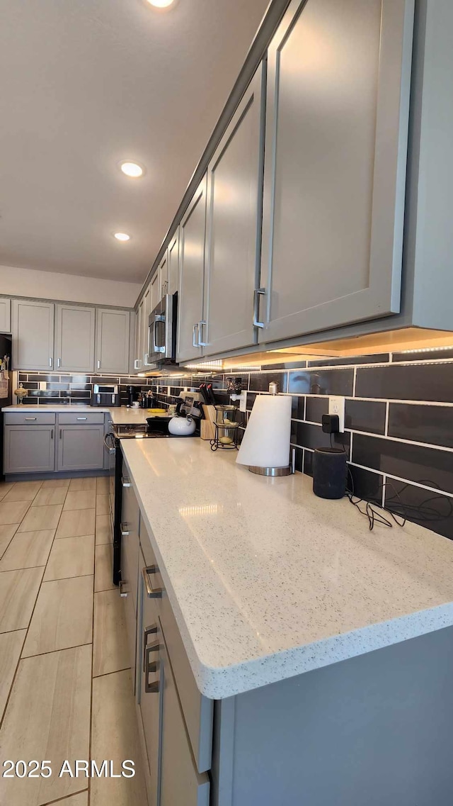 kitchen with light stone countertops, electric range, gray cabinets, and refrigerator