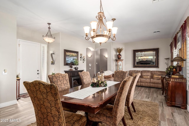 dining room with visible vents, baseboards, a chandelier, light wood-type flooring, and arched walkways