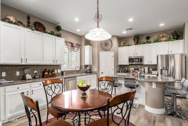 kitchen with tasteful backsplash, visible vents, light wood-type flooring, stainless steel appliances, and white cabinetry