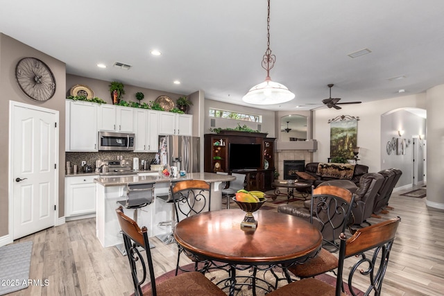 dining area with arched walkways, visible vents, a fireplace, and light wood-type flooring