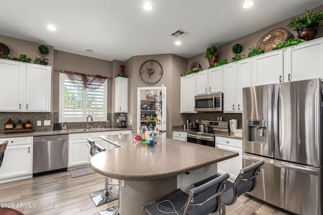 kitchen with a sink, a kitchen breakfast bar, appliances with stainless steel finishes, and white cabinetry