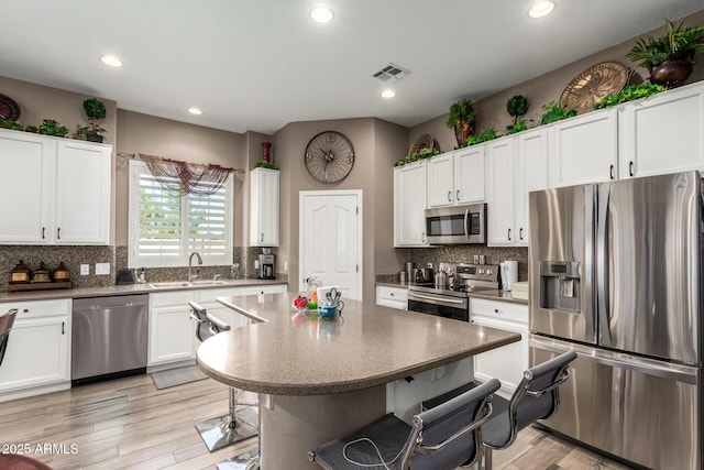 kitchen featuring backsplash, a kitchen bar, stainless steel appliances, white cabinetry, and a sink