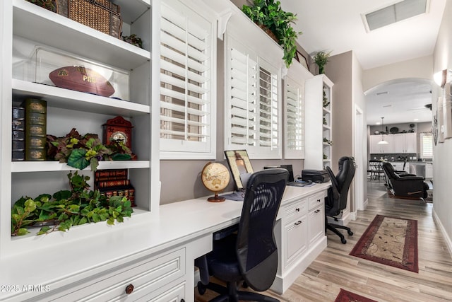 office area with visible vents, arched walkways, built in desk, and light wood finished floors