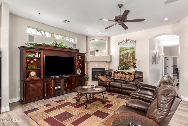 living area featuring light wood-style flooring, a fireplace, visible vents, and arched walkways