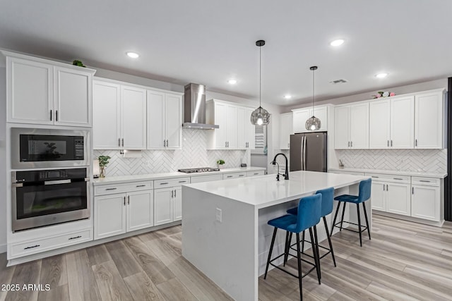 1501 E Rakestraw Ln, Gilbert, AZ 85298 - kitchen featuring appliances with stainless steel finishes, wall chimney range hood, tasteful backsplash, a kitchen breakfast bar, and light wood-type flooring