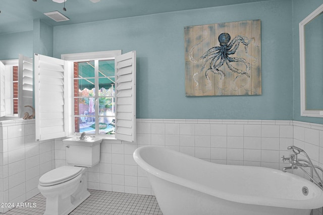 bathroom featuring toilet, a tub to relax in, tile patterned floors, and tile walls