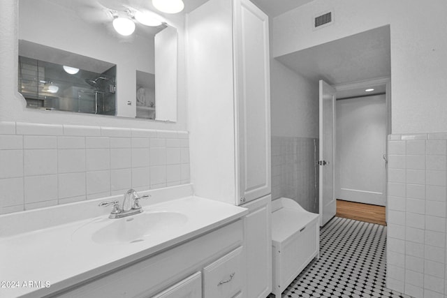 bathroom featuring a shower, tile patterned flooring, vanity, and tile walls