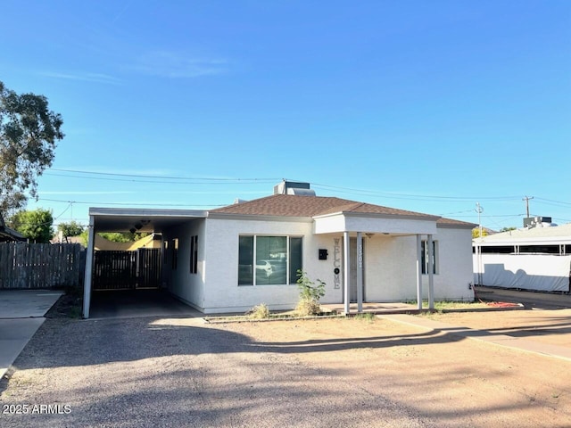 view of front of property with stucco siding, fence, a carport, and driveway