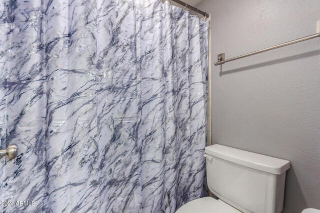 bathroom featuring a shower with curtain, toilet, and a textured wall