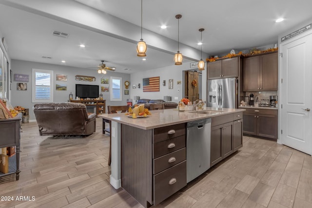 kitchen with appliances with stainless steel finishes, hanging light fixtures, sink, ceiling fan, and a kitchen island with sink