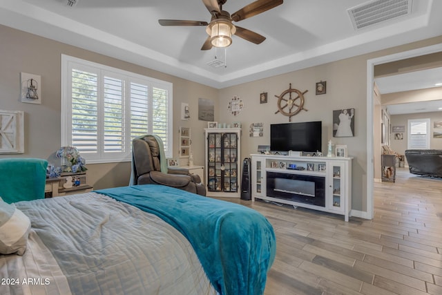 bedroom with light wood-type flooring, ceiling fan, and a raised ceiling