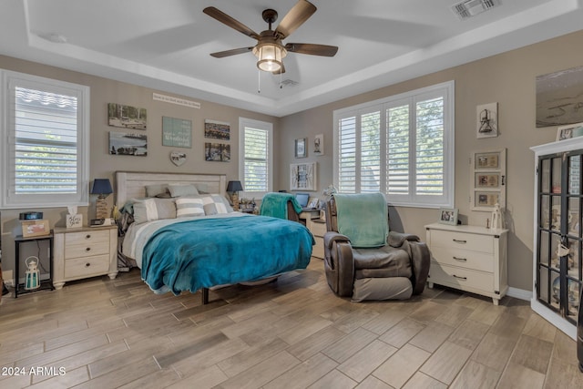 bedroom with multiple windows, ceiling fan, and a tray ceiling