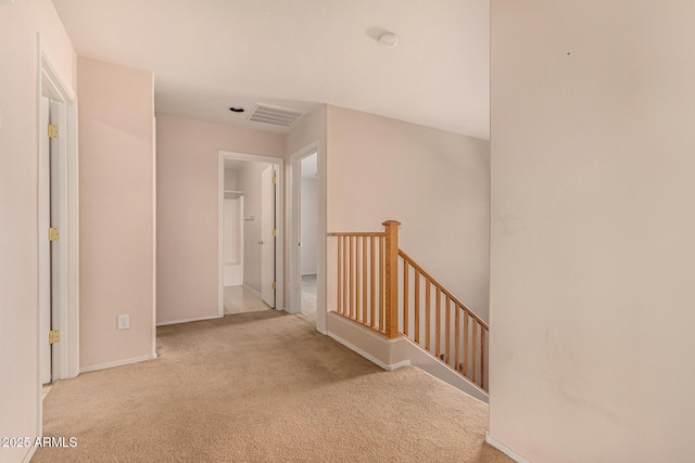 hall with carpet flooring, an upstairs landing, visible vents, and baseboards