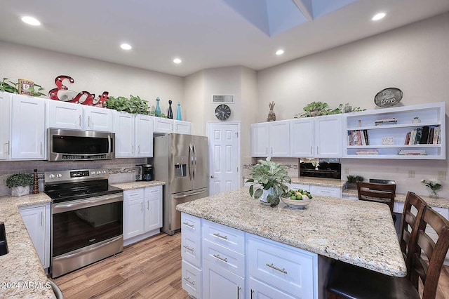 kitchen with tasteful backsplash, appliances with stainless steel finishes, light stone countertops, light hardwood / wood-style floors, and white cabinets