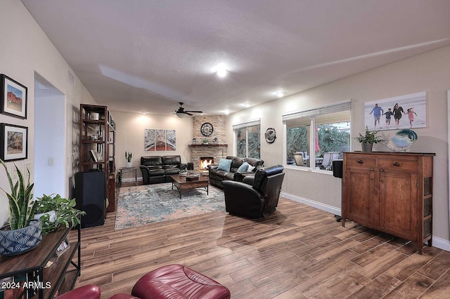 living room with a textured ceiling, wood-type flooring, ceiling fan, and a fireplace