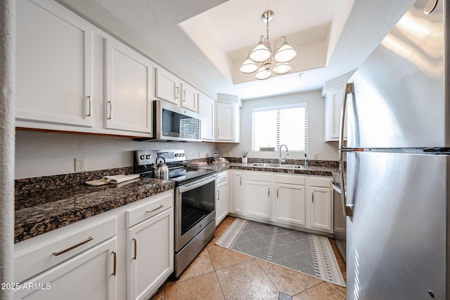 kitchen featuring a notable chandelier, stainless steel appliances, a sink, white cabinets, and a tray ceiling