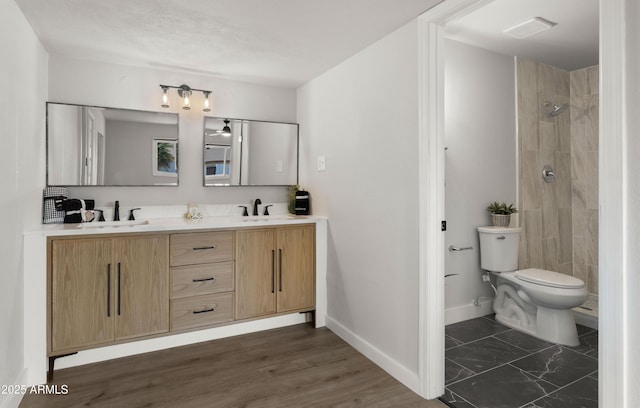 full bathroom with double vanity, toilet, a tile shower, and a sink