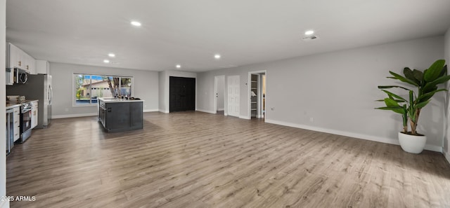 unfurnished living room featuring recessed lighting, baseboards, a sink, and light wood-style floors