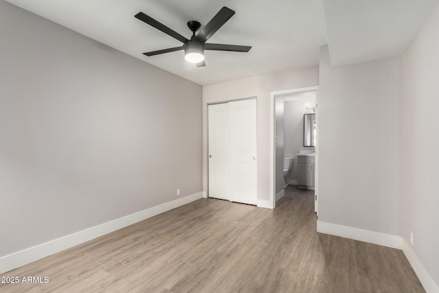 unfurnished bedroom with light wood finished floors, a closet, ensuite bathroom, a ceiling fan, and baseboards