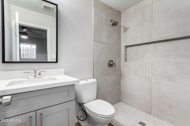 full bathroom with toilet, visible vents, a tile shower, and vanity