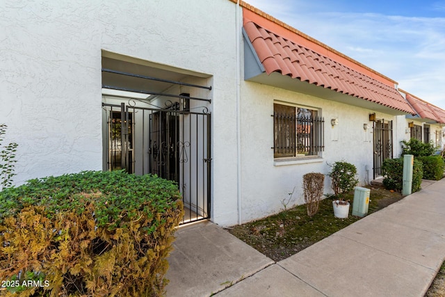 exterior space with a tile roof, a gate, and stucco siding