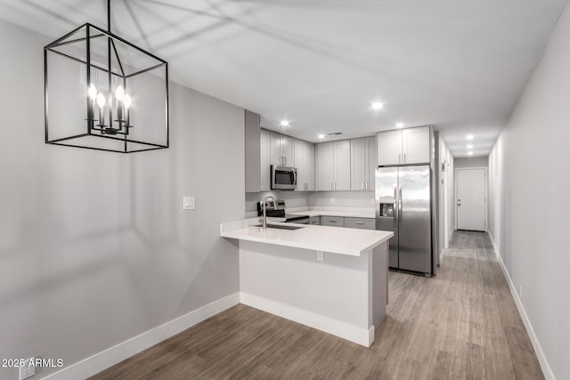 kitchen with a peninsula, stainless steel appliances, a sink, light countertops, and pendant lighting