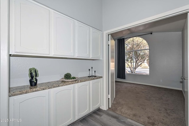 bar with white cabinets, dark stone counters, and carpet