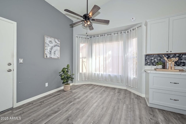 unfurnished dining area featuring ceiling fan, light wood-type flooring, and vaulted ceiling