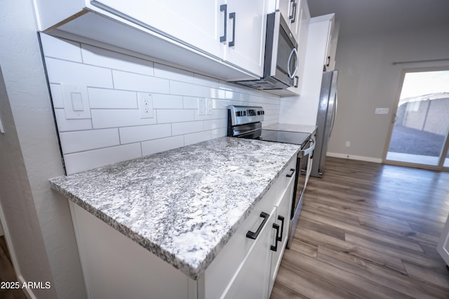 kitchen featuring dark wood-type flooring, white cabinetry, light stone counters, appliances with stainless steel finishes, and decorative backsplash