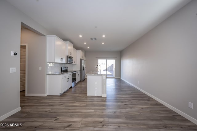 kitchen featuring appliances with stainless steel finishes, an island with sink, sink, white cabinets, and decorative backsplash