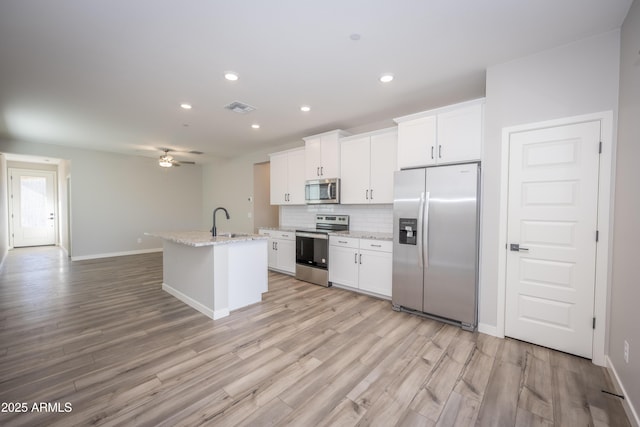 kitchen with sink, stainless steel appliances, light stone counters, an island with sink, and white cabinets