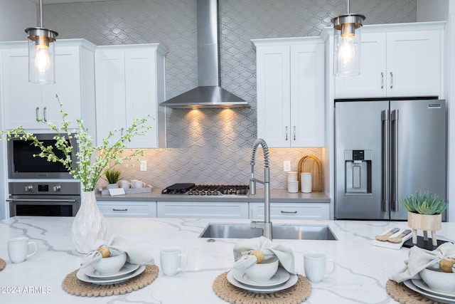 kitchen with white cabinets, backsplash, stainless steel appliances, wall chimney range hood, and decorative light fixtures