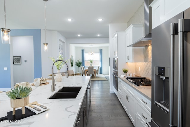 kitchen with pendant lighting, appliances with stainless steel finishes, backsplash, dark wood-type flooring, and wall chimney range hood