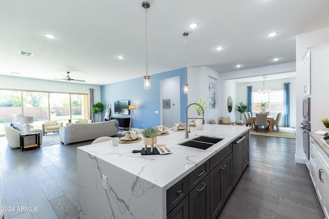 kitchen featuring decorative light fixtures, white cabinetry, ceiling fan with notable chandelier, dark wood-type flooring, and a center island with sink