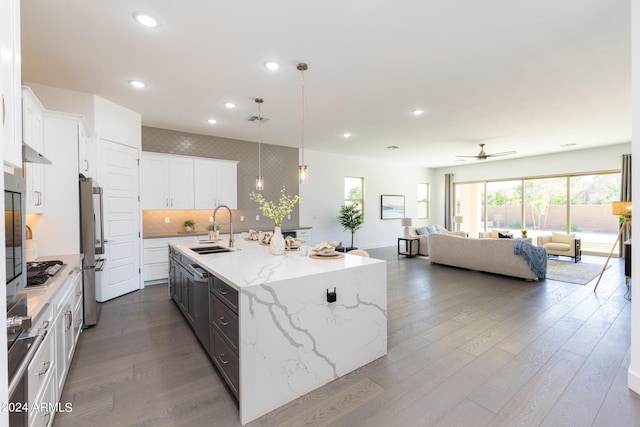 kitchen featuring decorative light fixtures, dark wood-type flooring, white cabinetry, a kitchen island with sink, and sink