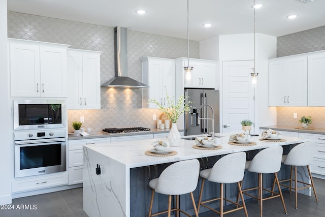 kitchen featuring pendant lighting, a center island with sink, appliances with stainless steel finishes, and wall chimney range hood