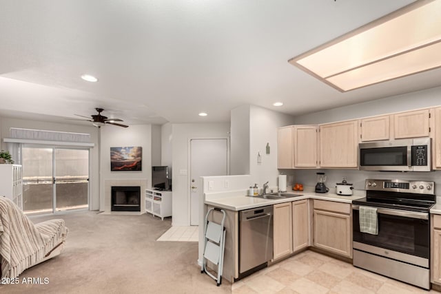 kitchen featuring light brown cabinetry, open floor plan, stainless steel appliances, and a sink