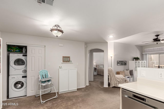 kitchen featuring visible vents, stacked washer and clothes dryer, stainless steel dishwasher, arched walkways, and light colored carpet