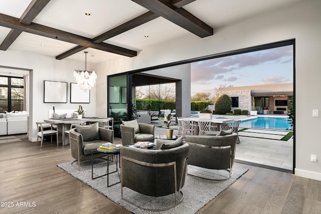 living area featuring beamed ceiling, coffered ceiling, wood finished floors, an inviting chandelier, and baseboards