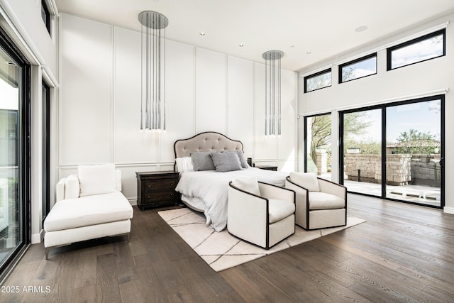 bedroom with access to exterior, a decorative wall, a high ceiling, and hardwood / wood-style floors