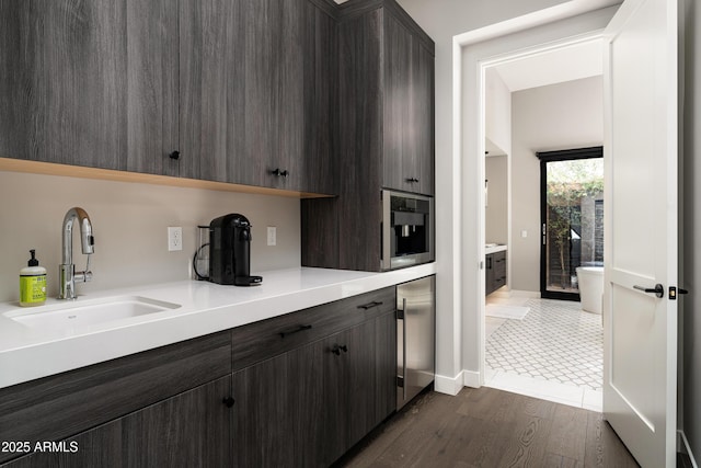 kitchen featuring dark brown cabinetry, wine cooler, light countertops, dark wood-style floors, and a sink