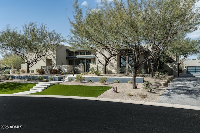 view of front of property featuring stucco siding, decorative driveway, and a front yard