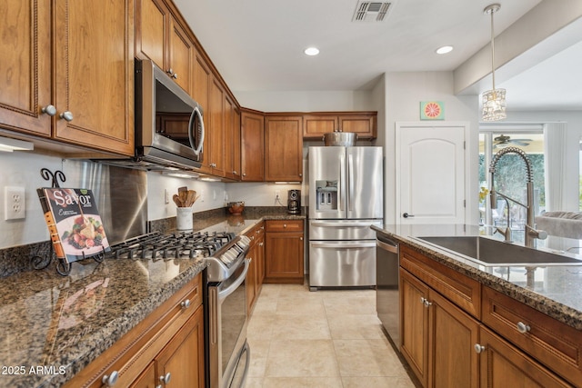 kitchen featuring visible vents, dark stone counters, appliances with stainless steel finishes, brown cabinetry, and a sink