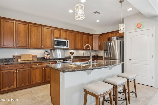 kitchen featuring visible vents, dark stone counters, brown cabinetry, stainless steel appliances, and a sink