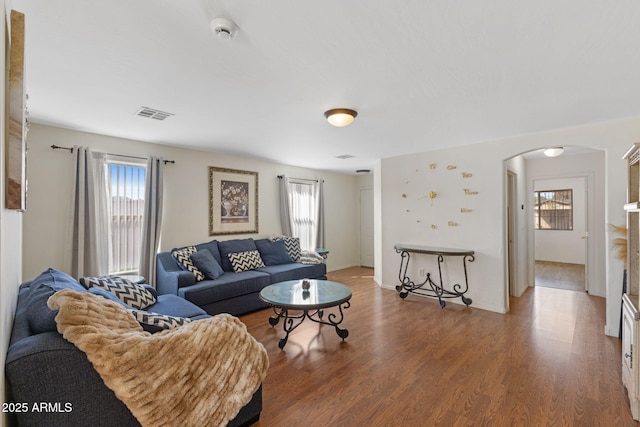 living area with visible vents, arched walkways, and wood finished floors