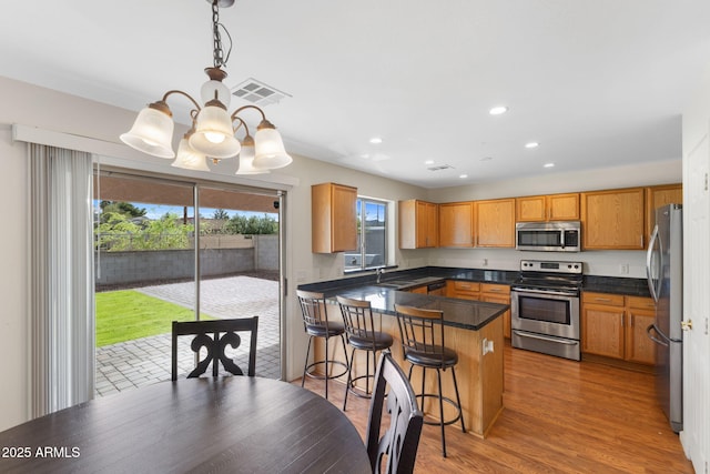 kitchen featuring visible vents, an inviting chandelier, dark countertops, a peninsula, and stainless steel appliances
