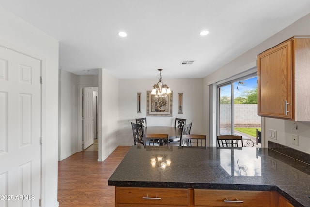 kitchen with an inviting chandelier, a peninsula, recessed lighting, wood finished floors, and decorative light fixtures