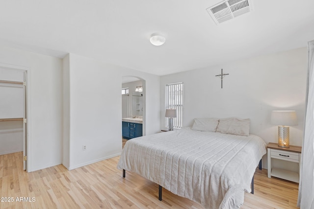 bedroom with light wood-style flooring, arched walkways, a spacious closet, visible vents, and baseboards